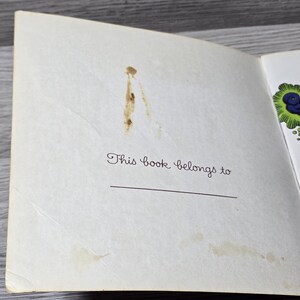 Puede incluir: P&aacute;gina de libro abierta con el texto "This book belongs to" en fuente cursiva. Una l&iacute;nea horizontal est&aacute; debajo del texto para un nombre. La p&aacute;gina tiene manchas marrones y est&aacute; ligeramente amarillenta.