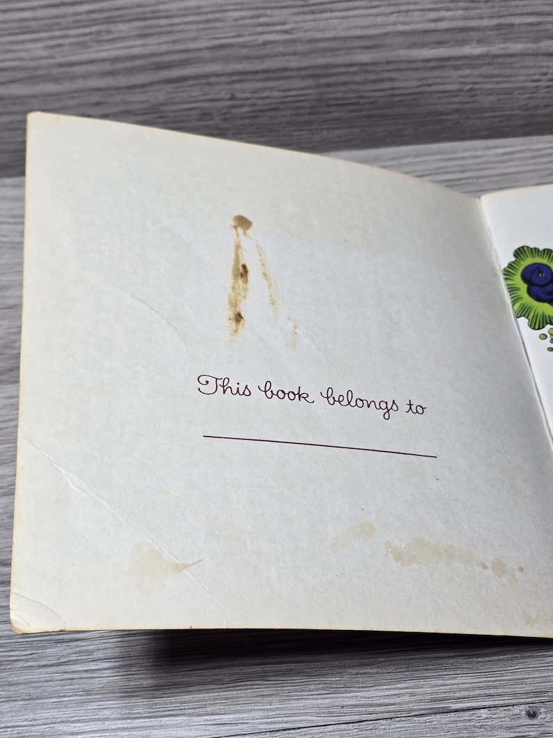 Puede incluir: P&aacute;gina de libro abierta con el texto "This book belongs to" en fuente cursiva. Una l&iacute;nea horizontal est&aacute; debajo del texto para un nombre. La p&aacute;gina tiene manchas marrones y est&aacute; ligeramente amarillenta.