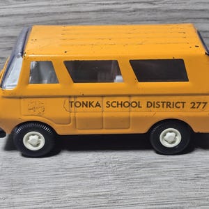 May include: A vintage yellow Tonka school bus toy with black tires and white hubcaps. The text "TONKA SCHOOL DISTRICT 277" is printed on the side. The toy bus has rectangular windows and a silver roof.