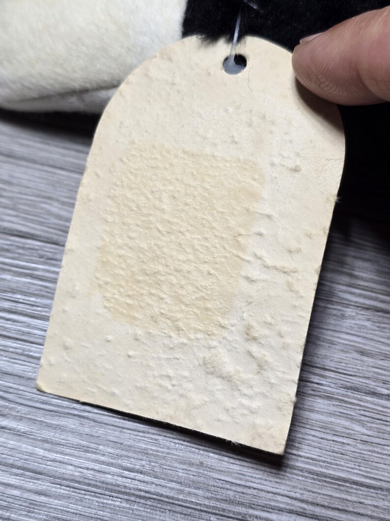 May include: A blank white tag with a hole punched in the top. The tag is attached to a black and white stuffed animal.