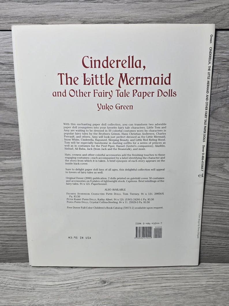 May include: A paperback book titled "Cinderella, The Little Mermaid and Other Fairy Tale Paper Dolls" by Yuko Green. The cover has a maroon title on a white background. The book contains paper dolls and costumes from various fairy tales.