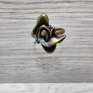 Puede incluir: Un anillo de tono dorado con un diseño abstracto estilizado. El anillo tiene un aspecto desgastado, antiguo.