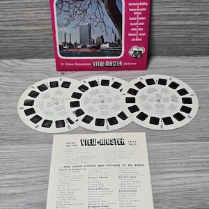 Könnte beinhalten: Eine Vintage View-Master-Spule mit einem Foto des UN-Gebäudes in New York City. Die Spule ist weiß mit schwarzem Text und Bildern. Der Text auf der Spule lautet "Your United Nations" und "New York".