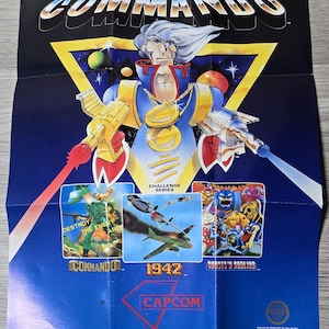 May include: A vintage CAPTAIN COMMANDO arcade game poster. The poster features a central character in a blue and yellow suit, holding futuristic weapons. Below are game scenes for Commando, 1942, and Ghosts 'n Goblins. The Capcom logo is at the bottom.