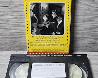 May include: A vintage VHS tape and box set for "The Invisible Ghost" horror film. The yellow box features the film's title and cast, with a black and white image. The VHS tape is black with a white label.