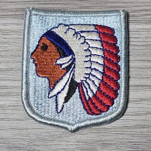May include: A blue embroidered patch with a Native American profile wearing a white and red feathered headdress.