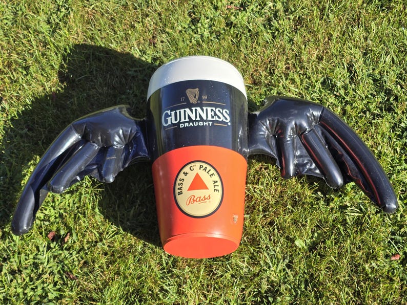 May include: A black inflatable beer stein with wings. The stein is decorated with the Guinness Draught logo and a Bass Pale Ale logo.