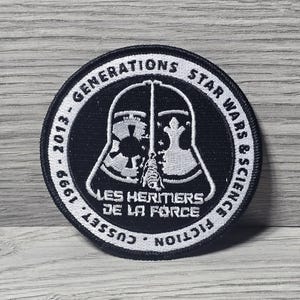 以下が含まれることがあります： ダース・ベイダーのヘルメットの様式化された画像が特徴の、丸い白黒のパッチ。「GENERATIONS STAR WARS & SCIENCE」と「LES HERITIERS DE LA FORCE」の文字と1999年から2013年の年号が記載されています。