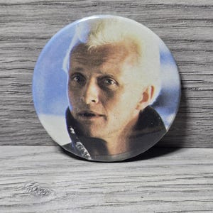 Puede incluir: Una taza de cerámica blanca con un asa negra y el texto "But First, Coffee" en un estilo manuscrito. La taza está sobre una superficie blanca.