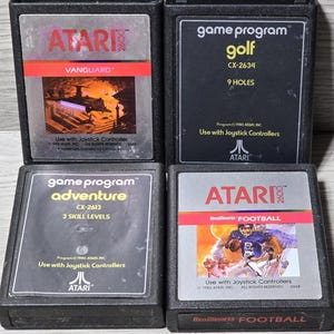 Op de afbeelding: Vier Atari 2600 spelcartridges. Titels zijn "Vanguard", "Golf", "Adventure" en "RealSports Football". Elke cartridge heeft een zwarte plastic behuizing met kleurrijke labels. De "RealSports Football" cartridge heeft een afbeelding van een footballspeler.