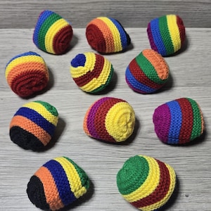 May include: Eleven small, round, crocheted balls featuring horizontal stripes in various vibrant colors including red, orange, yellow, green, blue, and purple. Each soft, handmade textile object displays a consistent knit pattern and rounded shape.