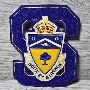 May include: A large, dark blue felt letter S patch featuring a central shield emblem. The shield displays a gold crown, a white beaver, and a blue tree on a yellow background. A white banner at the bottom contains the text SCITE ET STRENUE.
