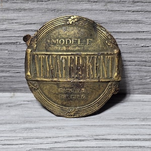 May include: A gold-colored metal badge with the text "MODEL E ATWATER KENT PATENTS PENDING" embossed on it.