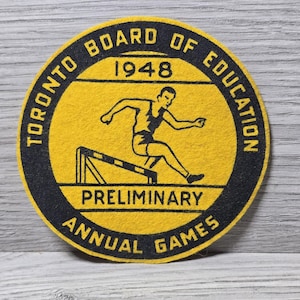 May include: A vintage yellow and black felt patch from the Toronto Board of Education, 1948. The circular patch features a hurdler in motion over a hurdle, with text that reads "Preliminary Annual Games."