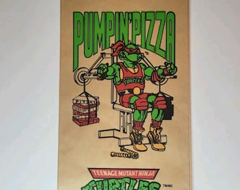 May include: Brown paper lunch bag featuring a Teenage Mutant Ninja Turtle character lifting weights, with the text "PUMPIN' PIZZA" in green. The bag also includes the text "TEENAGE MUTANT NINJA TURTLES".