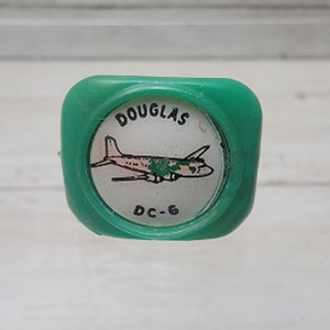 May include: A green plastic button with a white circle in the centre. The circle has a drawing of a Douglas DC-6 aircraft and the text "DOUGLAS DC-6".