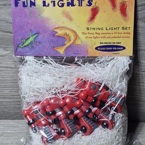 May include: A package of "Fun Lights" string lights. The package features a colorful design with the text "Fun Lights" and illustrations of a lizard, fish, and chili peppers. The string lights are red and black.