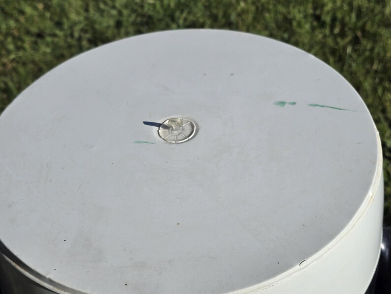 May include: White plastic lid with a small, round, clear plastic plug in the center. The lid has a few light green marks on the surface.