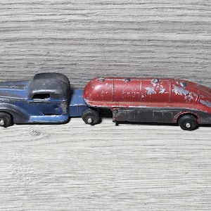 May include: Vintage toy truck and tanker in blue, red, and black. The truck has a blue cab and a black roof. The tanker is red with black accents. The toy shows signs of wear.
