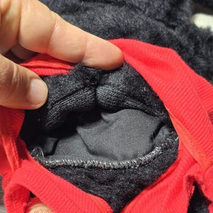 May include: Close-up of the inside of a black and red Mickey Mouse plush toy. The toy has a zipper and a label that reads "Mickey Mouse" and "Instructions".