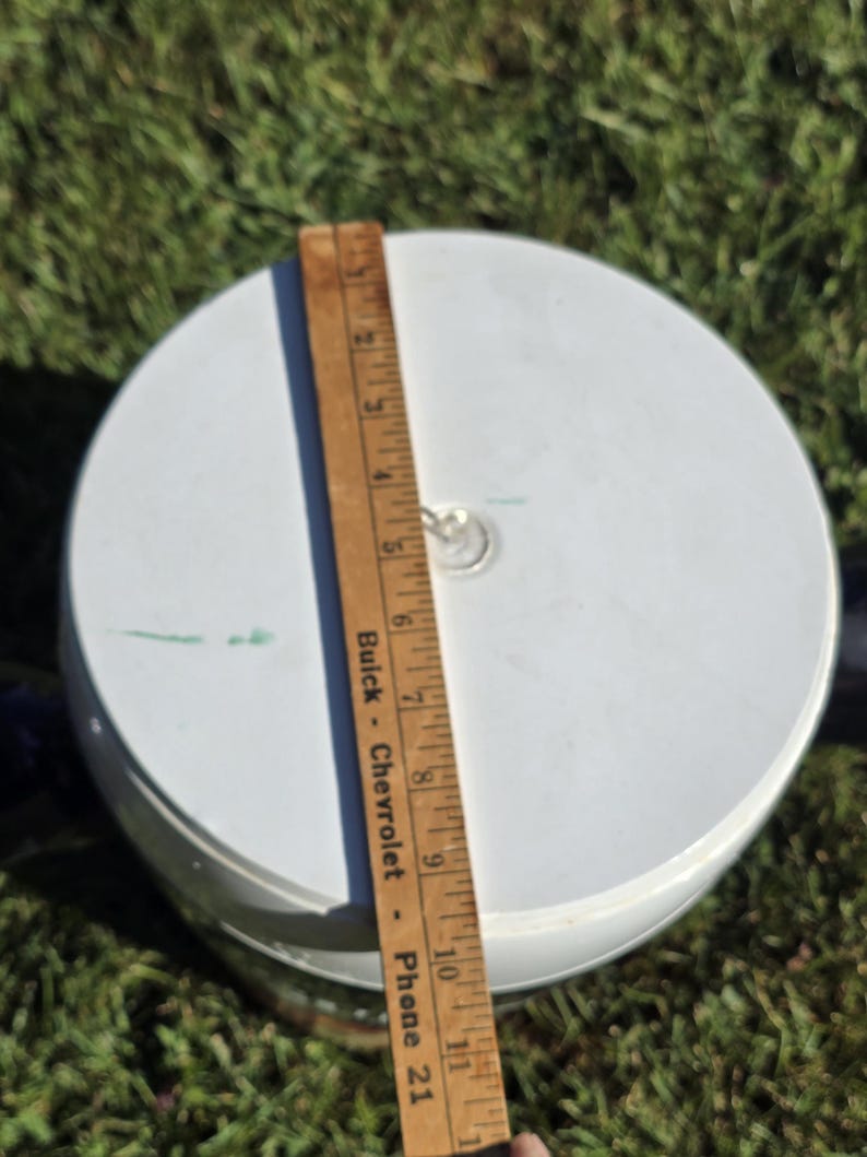 May include: White plastic lid with a metal ring handle. A wooden ruler with the text "Buick - Chevrolet - Phone 21" is next to the lid.