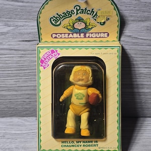 Könnte beinhalten: Vintage Cabbage Patch Kids Chauncey Robert-Figur in Originalverpackung. Die Figur trägt eine gelbe Football-Uniform und hält einen roten Football. Die Box ist gelb und grün mit den Worten "First Edition" und "Poseable Figure".