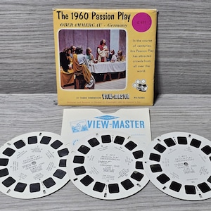 Könnte beinhalten: Ein Vintage View-Master-Set mit "The 1960 Passion Play" aus Oberammergau, Deutschland. Das Set enthält eine gelbe Box mit einer Spielszene, eine View-Master-Karte und drei kreisförmige Rollen mit Bildern. Der Text auf der Box lautet "21 Three Dimension Pictures".
