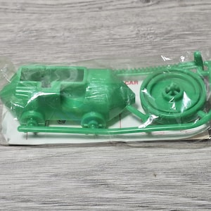 Puede incluir: Un kit de coche de juguete de plástico verde, aún en su embalaje original. El kit incluye la carrocería, las ruedas y otros componentes. El coche es de color verde brillante y sólido. El embalaje es de plástico transparente.
