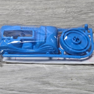 May include: A blue plastic model kit of a motorcycle, still in its original packaging. The kit includes various parts, such as the frame, wheels, and other components, ready for assembly. The parts are a vibrant shade of blue.