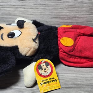May include: A black and red plush Mickey Mouse puppet with a yellow circle on the red shorts. The puppet has a tag that says "Come alive Puppet toy Two toys in one Mickey Mouse Club".