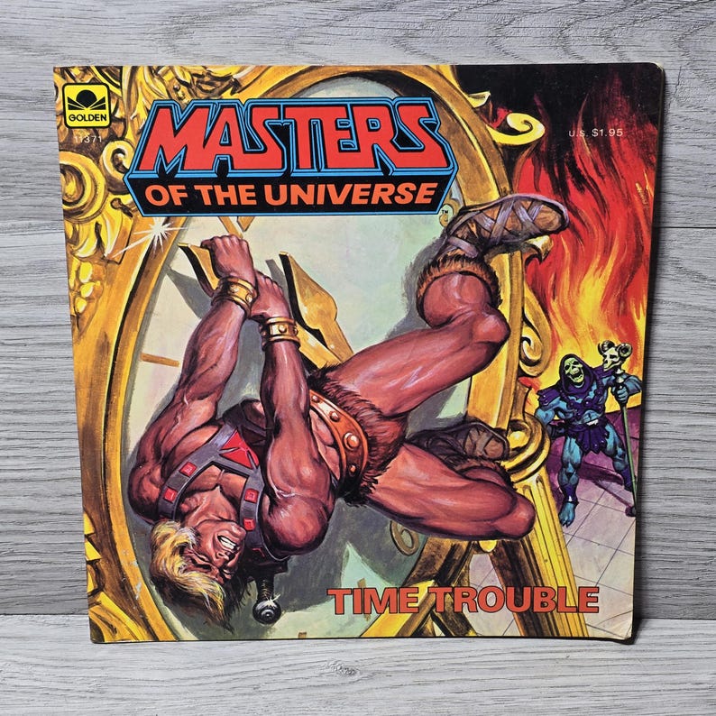 Puede incluir: Una portada de c&oacute;mic vintage de "Masters of the Universe". La portada presenta un personaje musculoso colgando de un reloj, con el t&iacute;tulo "Time Trouble". El fondo incluye una esfera de reloj, llamas y otros personajes.