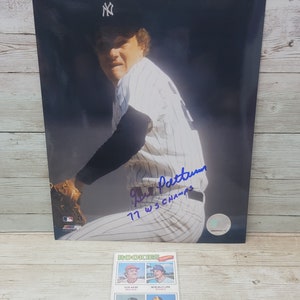May include: A black and white photo of a baseball player wearing a New York Yankees uniform. The player is holding a baseball glove and is in a pitching stance. The photo is signed by the player, Gil Patterson, and includes the text "77 WS CHAMPS".
