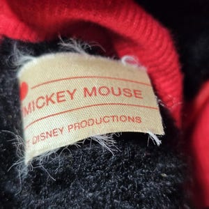 May include: Close-up of a black and red plush toy with a white label that reads "Mickey Mouse Disney Productions".