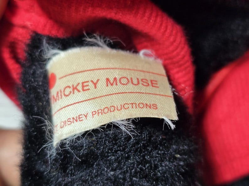 May include: Close-up of a black and red plush toy with a white label that reads "Mickey Mouse Disney Productions".
