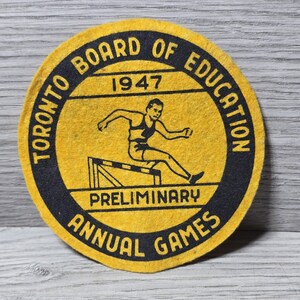 May include: A vintage yellow and black felt patch from the Toronto Board of Education. The patch features text that reads "Toronto Board of Education 1947 Preliminary Annual Games" around the perimeter. A black silhouette of a hurdler is in the center.
