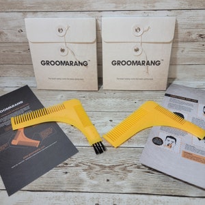 Könnte beinhalten: Zwei gelbe Bartpflegewerkzeuge mit schwarzen Borsten und einem Kamm auf jedem Werkzeug. Die Werkzeuge befinden sich auf einer Holzoberfläche mit zwei weißen Umschlägen mit dem Text "Groomarang". Der Text "The best styling comb that helps keep going back" befindet sich auf den Umschlägen. Ein schwarz-weißes Anleitungsblatt mit dem Text "Directions for Use" befindet sich ebenfalls auf der Oberfläche.