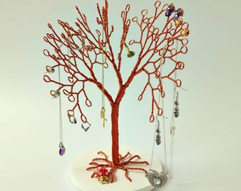 Könnte beinhalten: Ein dekorativer Schmuckhalter in Form eines kupferfarbenen Drahtbaums mit weißer, kreisförmiger Basis. Der Baum hält verschiedene Halsketten, Ohrringe und Ringe. Eine Marienkäferfigur befindet sich am Fuß des Baumes. Der Schmuckhalter ist einzigartig.