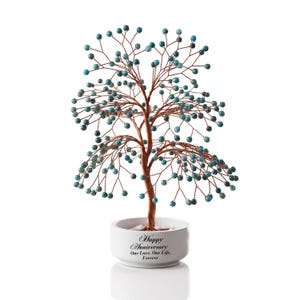 Peut inclure: Une sculpture d'arbre en fil métallique avec des branches couleur cuivre ornées de petites perles en pierre bleu sarcelle. L'arbre est fixé sur une base ronde en céramique blanche avec le texte noir : Happy Anniversary, One Love, One Life, Forever.