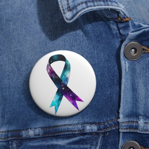 May include: A white button featuring a galaxy-themed ribbon in shades of blue, purple, and black. The ribbon is tied in a loop and is a symbol of awareness and support.