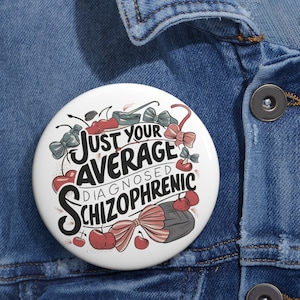 May include: A white button with a black and red design. The button features the text "Just your average diagnosed schizophrenic" with cherries, bows, and other decorative elements.