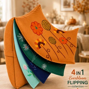 May include: A 4-in-1 Everbloom Flipping collection pillow featuring four distinct fabric layers. The top layer is orange with floral graphics. Beneath are dark green, navy blue, and light blue layers decorated with snowflakes and tulips.