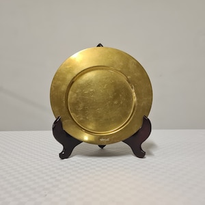 Peut inclure: Une assiette de service en métal doré sur un support en bois brun foncé. L'assiette a un bord légèrement surélevé et une surface lisse.