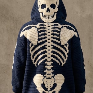Könnte beinhalten: Ein dunkelblauer Häkel-Kapuzenpullover mit einem großen, cremeweißen Skelett-Design auf der Rückseite. Die Kapuze zeigt einen detaillierten Totenkopf, während das Rückenteil den Brustkorb, die Wirbelsäule und das Becken in Kontrastgarn zeigt.