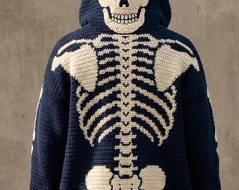 May include: A dark navy blue crochet hoodie featuring a large, off-white skeleton design on the back. The hood displays a detailed skull, while the back panel shows the rib cage, spine, and pelvic bones in a contrasting cream-colored yarn.