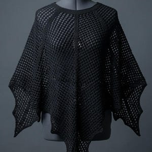 May include: A black crochet poncho featuring an open, grid-like stitch pattern throughout. The garment has a rounded neckline and a pointed, asymmetrical hemline that extends into distinct, angular points at the sides and center front.