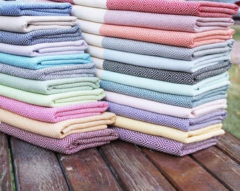 May include: A stack of colorful Turkish towels with a diamond pattern. The towels are folded and stacked in a variety of colors, including pink, blue, green, yellow, and red.