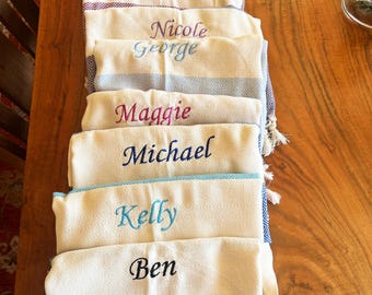 Può includere: Un mucchio di asciugamani bianchi con diversi nomi ricamati in colori diversi, tra cui Ben, Kelly, Michael, Maggie, George, Nicole e Anna.