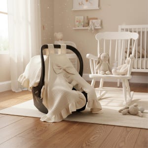 May include: Cream-colored baby car seat cover with a large bow and ruffled edges. A white rocking chair with two stuffed bunny toys sits nearby. The nursery setting includes a crib and decorative items, creating a soft, inviting atmosphere.