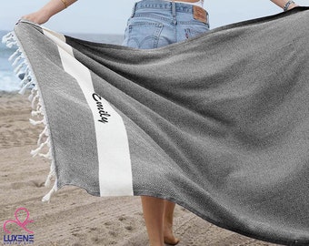 Può includere: Un asciugamano da spiaggia a strisce bianche e nere con il nome "Emily" ricamato. L'asciugamano è in cotone e ha un bordo a frange.