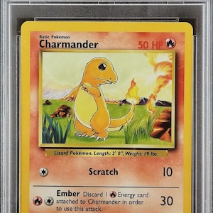 May include: A 1999 Pokemon trading card featuring Charmander, a lizard Pokemon with orange skin and a flame tail. The card is in mint condition and has a PSA grading of 9. The card text reads "Basic Pokemon Charmander 50 HP" and "Lizard Pokemon. Length: 2' 0", Weight: 19 lbs."
